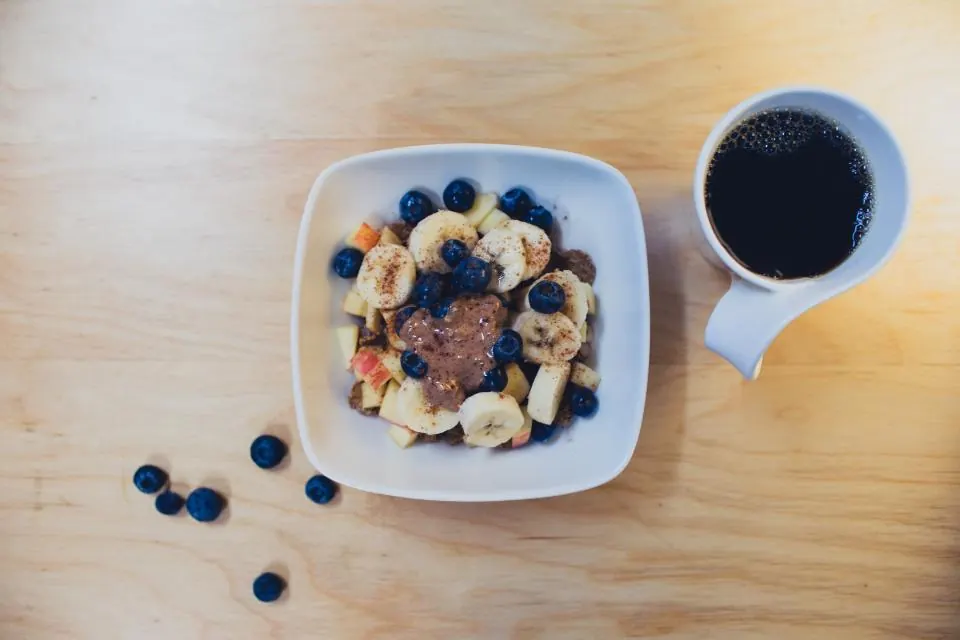 Desayuno con plátano, arándanos y café sobre una mesa de madera