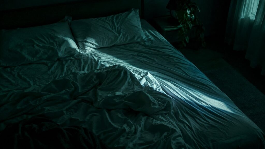 Cama deshecha en un dormitorio a oscuras, iluminada apenas por un haz de luz de luna que cruza las sábanas de madrugada
